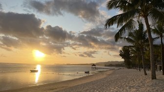 Ein malerischer Strand bei Sonnenuntergang, mit sanften Wellen und einer kleinen Boot auf dem Wasser.