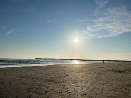 Ein ruhiger Strand bei Sonnenuntergang, mit sanften Wellen und einem klaren Himmel, der in warmen Farben leuchtet.