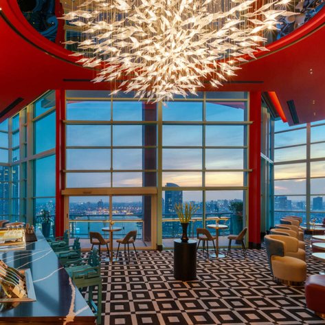 Elegante Restaurant mit atemberaubendem Blick auf die Skyline von Bangkok, beleuchtet von einer kunstvollen Deckenleuchte.