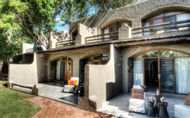 Eine moderne Lodge mit großen Fenstern und einem einladenden Außenbereich, umgeben von üppigem Grün und Bäumen.