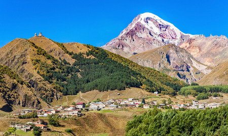 Die majestätischen Berge umgeben ein malerisches Dorf, während der schneebedeckte Gipfel im Hintergrund strahlt.