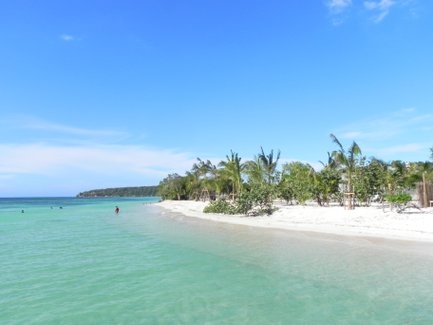 Ein ruhiger Strand mit feinem, weißem Sand und klarem, türkisfarbenem Wasser, umgeben von Palmen und üppiger Vegetation.