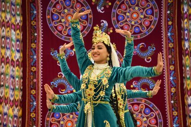 Eine Tänzerin in traditioneller Kleidung lächelt, während sie mit anmutigen Bewegungen auf einer Bühne tanzt.