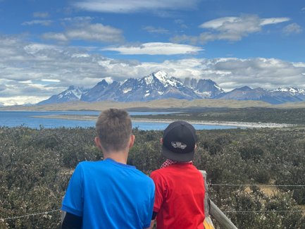 Zwei Kinder stehen am Ufer eines Sees und blicken auf die majestätischen Berge von Torres del Paine im Hintergrund.