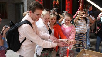 Eine Gruppe von Menschen steht in einem Tempel und zündet gemeinsam Räucherspiralen an, um ihre Wünsche zu äußern.