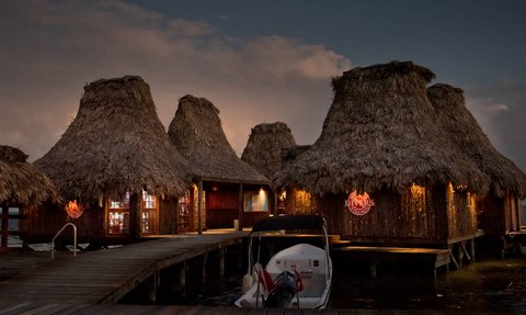 Die strohgedeckten Hütten des Resorts strahlen in der Dämmerung, während ein Boot am Steg festgemacht ist.