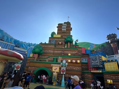 Ein lebhaftes Freizeitpark-Szenario mit einer bunten Mario Kart Attraktion und vielen Besuchern, die sich versammeln.