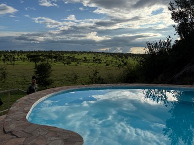 Ein klarer Pool spiegelt den Himmel und die Wolken wider, umgeben von einer grünen Landschaft und sanften Hügeln.
