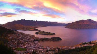 Ein atemberaubender Panoramablick auf Queenstown, umgeben von majestätischen Bergen und einem glitzernden See bei Sonnenuntergang.