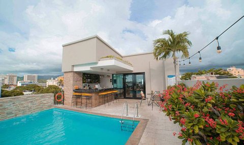 Ein stilvoller Poolbereich mit einer Bar, umgeben von tropischen Pflanzen und einem klaren blauen Himmel über Kolumbien.