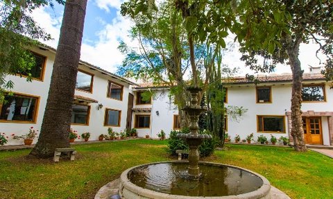 Ein malerischer Innenhof mit einem Brunnen, umgeben von einem gepflegten Garten und modernen Gebäuden im Hintergrund.