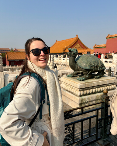 Eine junge Frau mit Sonnenbrille lächelt vor einer Statue einer Schildkröte in der Verbotenen Stadt in Peking.
