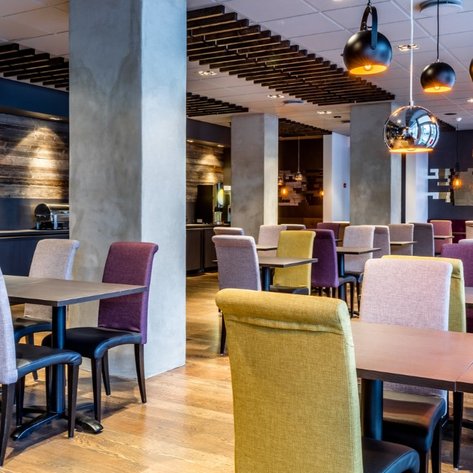 Ein modernes Restaurant mit stilvollen Tischen und bunten Stühlen, die eine einladende Atmosphäre schaffen.