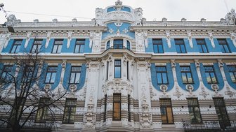 Die Fassade eines Jugendstilgebäudes in Riga zeigt kunstvolle Verzierungen und blaue Akzente unter einem bewölkten Himmel.