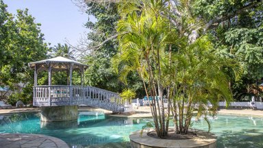 Ein malerischer Pool mit einer Holzbrücke und üppigem Grün umgibt die entspannende Atmosphäre des Resorts.