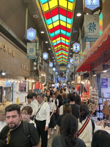 Ein belebter Markt in Kyoto mit bunten Lichtern und vielen Menschen, die durch die engen Gassen schlendern.
