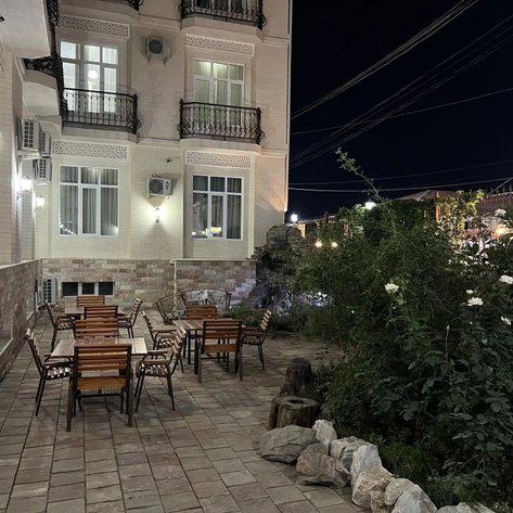 Ein gemütlicher Gartenbereich mit Holztischen und Stühlen, umgeben von Pflanzen, beleuchtet von sanften Lichtern in der Nacht.