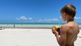 Junge genießt Kokoswasser direkt aus der Frucht am Strand von Puerto Morelos – Mexiko Familienreise