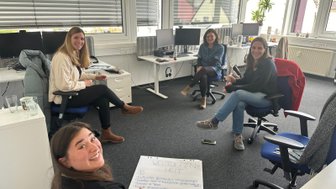 Vier Frauen sitzen in einem modernen Büro und diskutieren lebhaft über Ideen, während sie Notizen auf einem Blatt Papier machen.