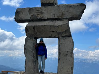 Eine Person steht in einem großen Steinskulptur, umgeben von einer beeindruckenden Berglandschaft und einem blauen Himmel.