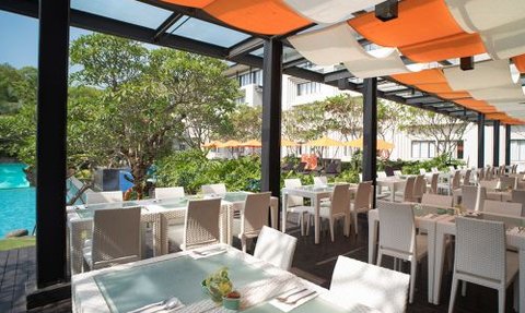 Ein eleganter Cafébereich mit weißen Tischen und Stühlen, umgeben von üppigem Grün und einem Pool im Hintergrund.