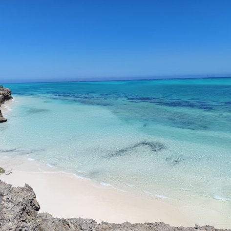 Ein atemberaubender Blick auf einen ruhigen Strand mit klarem, türkisfarbenem Wasser und sanften Wellen, umgeben von Felsen.