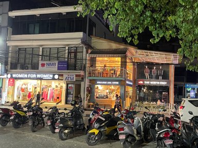 Eine belebte Straße in Pokhara mit verschiedenen Geschäften, darunter 'Women for Women' und 'The North Face'.