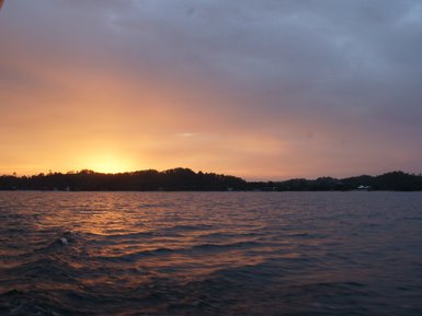 Ein atemberaubender Sonnenuntergang über dem Meer, mit sanften Wellen und einer bewölkten, farbenfrohen Himmelsszene.