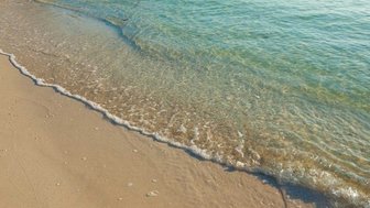 Sanfter Wellenlauf trifft auf den feinen Sandstrand, während das klare Wasser in der Sonne glitzert.