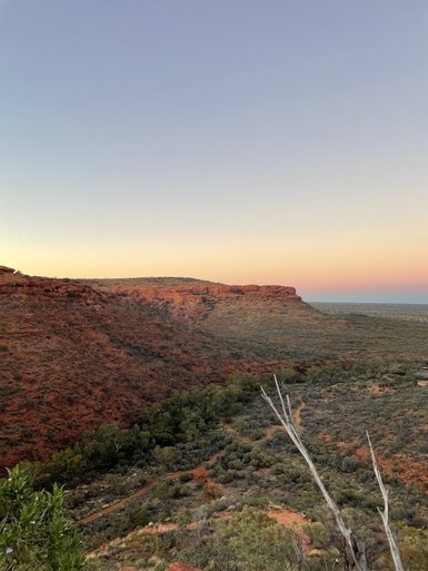 Ein weitläufiger Blick über die australische Wildnis, geprägt von roten Felsen und sanften Hügeln in der entfernten Kulisse.
