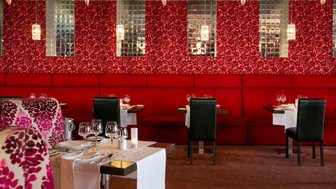 Elegante Restaurantansicht mit roten Wänden und stilvollen Tischen, die für ein feines Abendessen gedeckt sind.