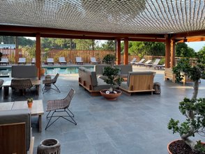 Ein eleganter Außenbereich mit modernen Möbeln, umgeben von Pflanzen und einem glitzernden Pool im Hintergrund.