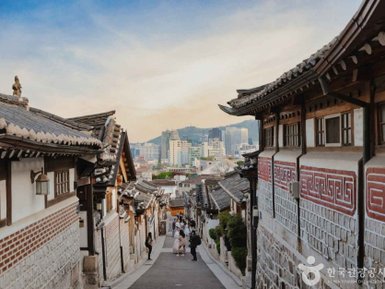 Eine malerische Straße in Bukchon Hanok Village, gesäumt von traditionellen koreanischen Häusern und modernen Gebäuden im Hintergrund.