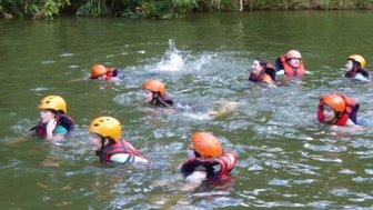 Eine Gruppe schwimmen mit Schwimmwesten durch einen Fluss