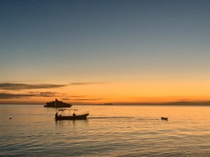 Ein ruhiger Sonnenuntergang über dem Meer, mit sanften Wellen und einem Boot, das langsam in der Ferne fährt.