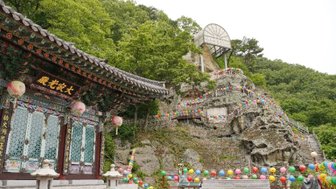 Ein traditionelles Gebäude mit bunten Laternen steht vor einer bewaldeten Felslandschaft, die mit festlichen Dekorationen geschmückt ist.