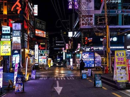 Eine belebte Straße in Gangnam, beleuchtet von bunten Neonlichtern und Werbetafeln, die das nächtliche Stadtleben zeigen.