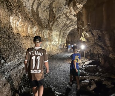Zwei Personen gehen durch einen dunklen Höhlengang, umgeben von beeindruckenden Felsformationen und schwachem Licht.