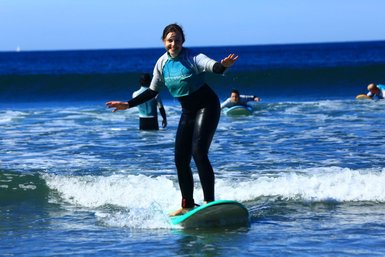 Eine Surferin balanciert auf ihrem Brett und genießt die Wellen an einem sonnigen Strandtag.