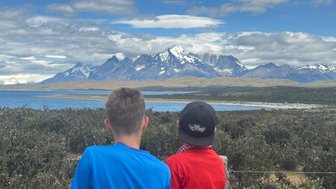 Zwei Kinder stehen am Ufer eines Sees und blicken auf die majestätischen Berge von Torres del Paine im Hintergrund.
