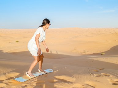 Teen beim Sandboarding auf einer Düne in der Wüste – Oman Familienreise