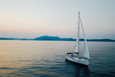 Ein Segelboot gleitet sanft über das ruhige Wasser, umgeben von sanften Hügeln im Hintergrund und einem zarten Abendhimmel.