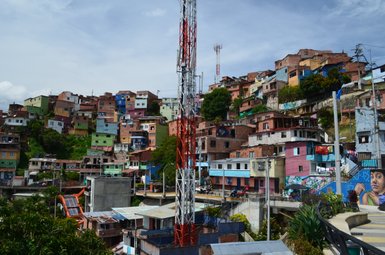 Bunte Häuser in Medellín, Comuna 13, erstrecken sich über einen Hügel, umgeben von grüner Vegetation und urbaner Infrastruktur.