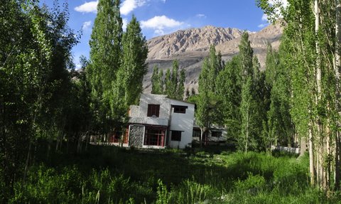Ein modernes, weißes Haus steht umgeben von hohen, grünen Bäumen und einer malerischen Berglandschaft im Hintergrund.