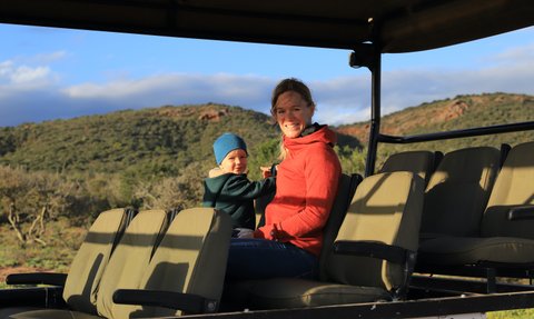 Mutter und Kind genießen gemeinsam die Safari im offenen Jeep und lächeln in die Kamera – Garden Route Reise mit Kindern