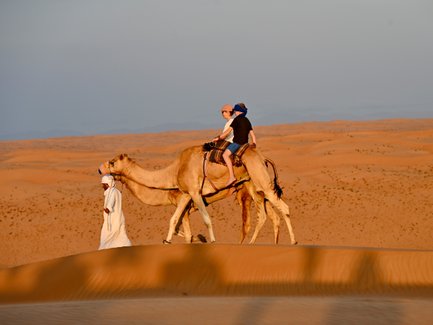 Beduin führt Kamele mit Mutter und Tochter durch die Wüste – Oman Familienreise