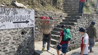Eine Gruppe von Kindern steht an einer steinernen Treppe, während ein Erwachsener mit einem Korb auf dem Rücken vorbeigeht.