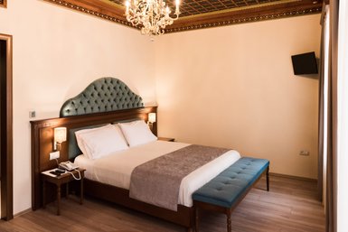 Ein elegantes Hotelzimmer mit einem großen, gepolsterten Bett und einem blauen Hocker am Fußende, umgeben von sanften Farben.