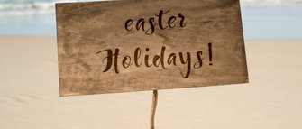 Ein Holzschild steht am Strand und verkündet fröhlich die Osterferien mit geschwungener Schrift.