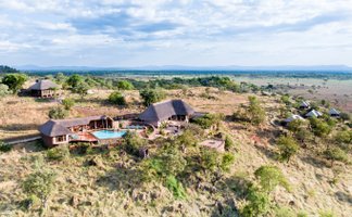 Eine atemberaubende Aussicht auf die Ikoma Hills Lodge, umgeben von sanften Hügeln und üppiger Vegetation in Tansania.